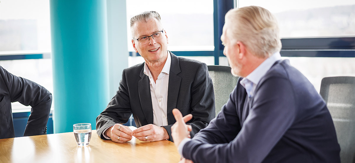 	Markus Schwarze, Horst Heckhorn and Martin Grunau from the CENIT leadership team are sitting at the corner of a conference table and listening to another person.	