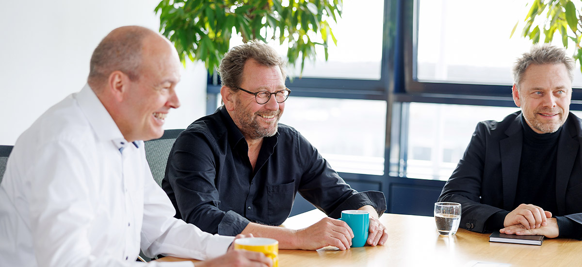 	Markus Schwarze, Horst Heckhorn and Martin Gruneau from the CENIT leadership team are sitting at the corner of a conference table and listening to another person.	